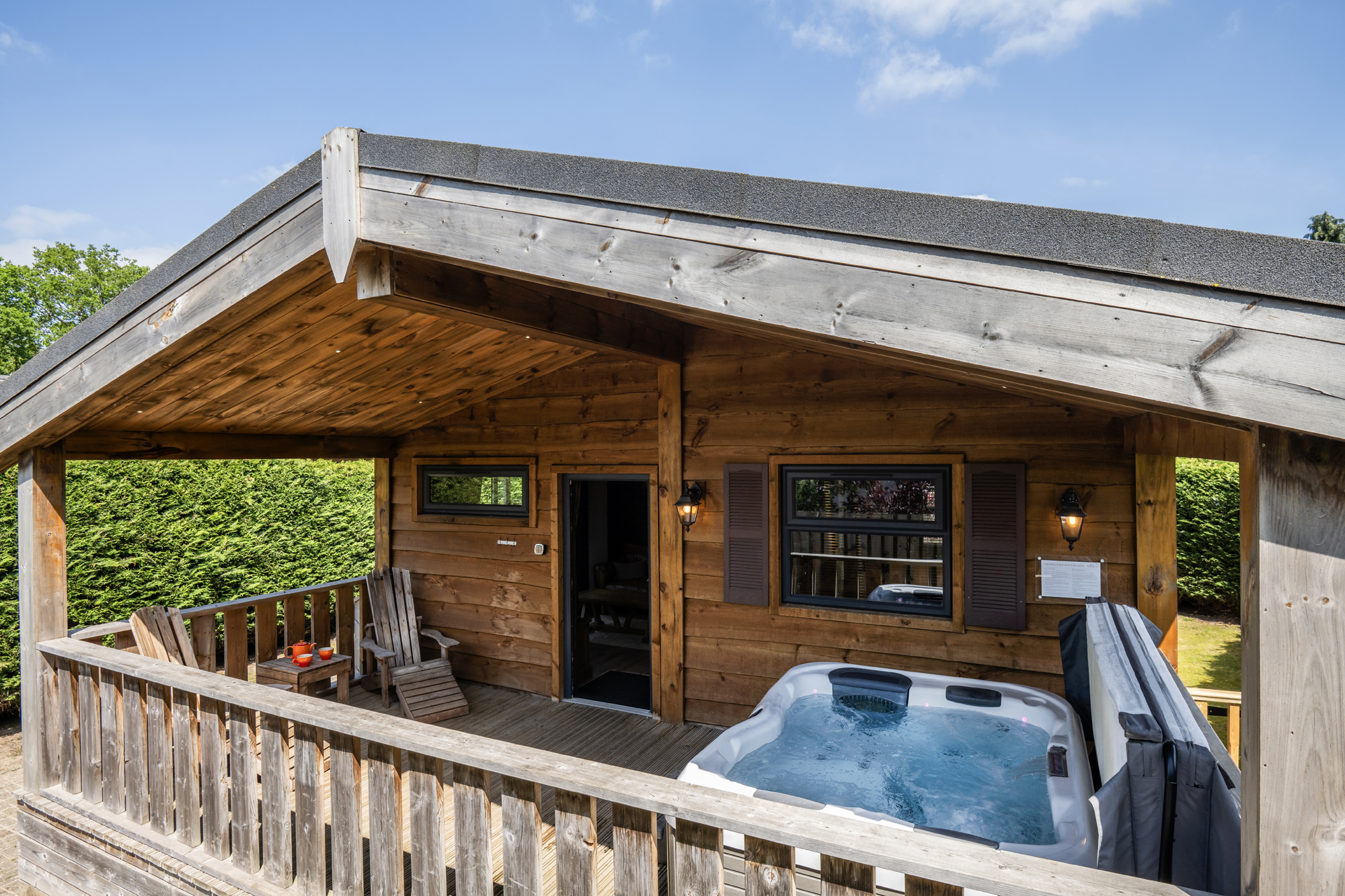 Wood cabin porch with a hot tub on the deck, wooden railing, and a clear blue sky above.